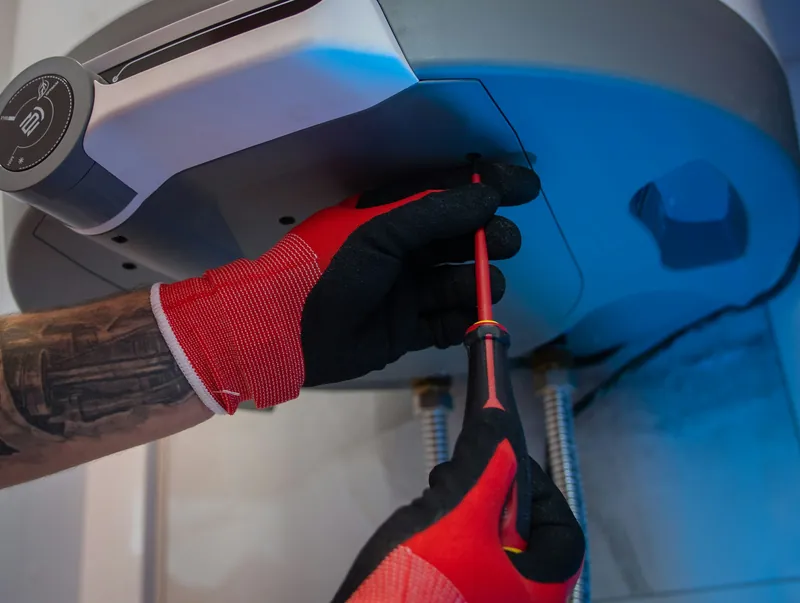 Gloved hands with a screwdriver at the control panel of a water heater