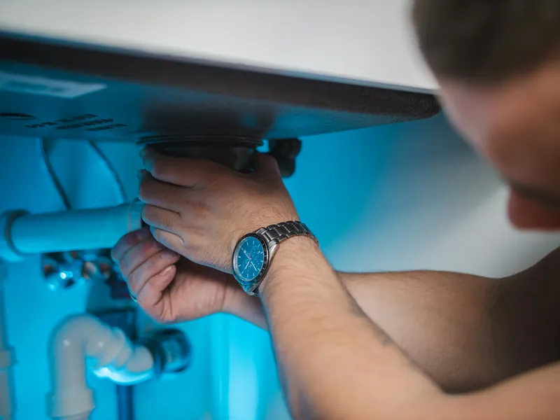 Hands tightening a pipe fitting under a sink