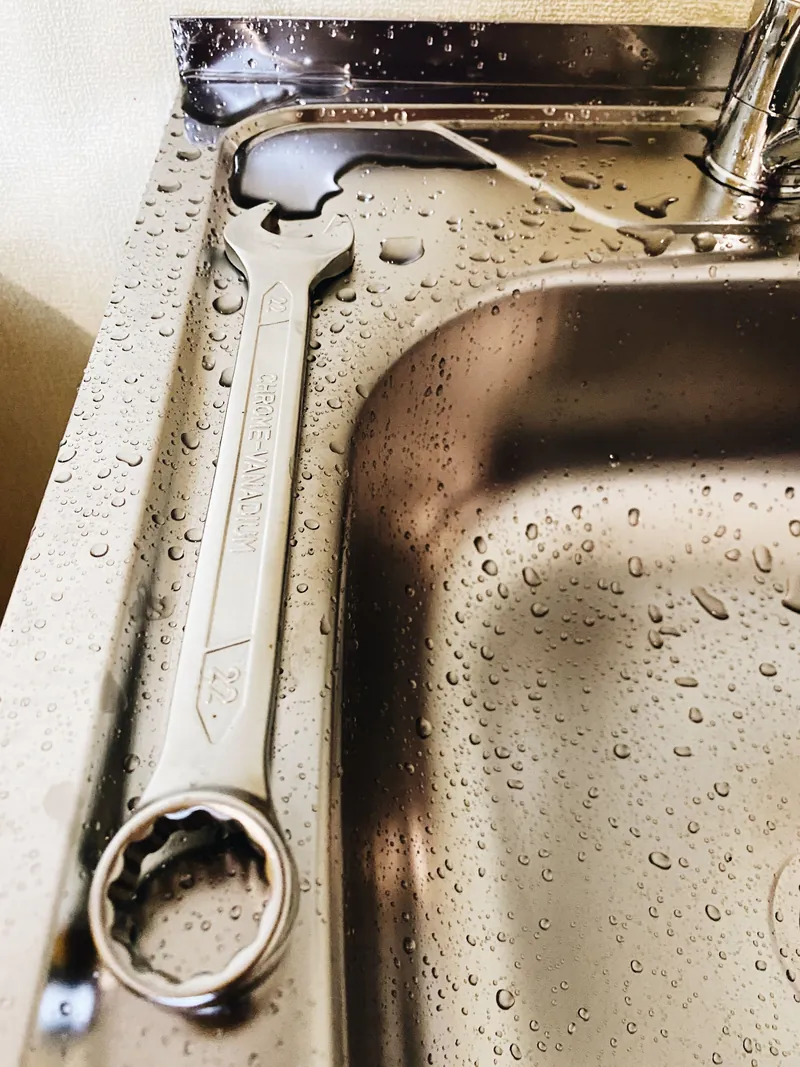A spanner lying on the edge of a wet stainless steel kitchen sink