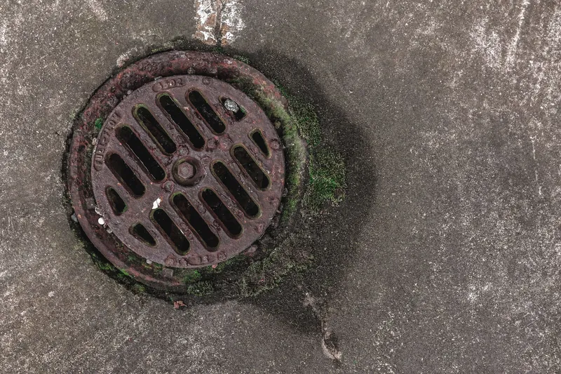 A rusted cast-iron drain grid set in a concrete yard
