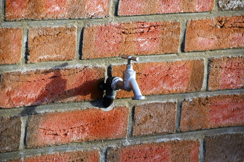 A chrome garden tap on a red face-brick wall