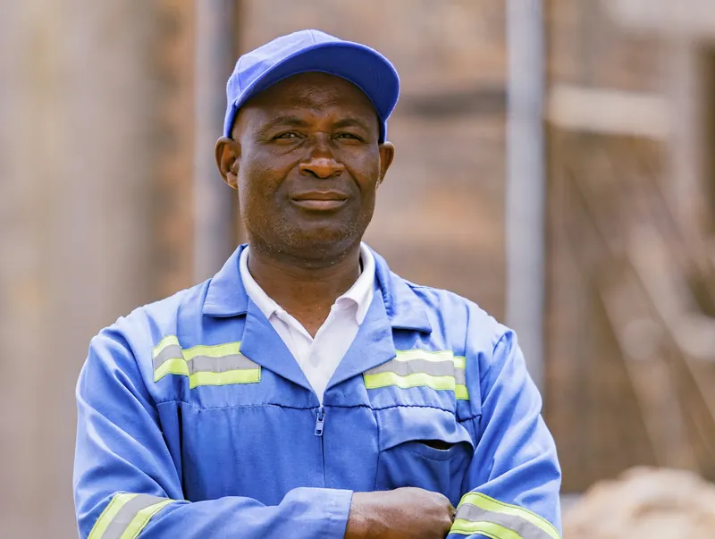 A plumber in blue overalls with reflective strips, arms folded