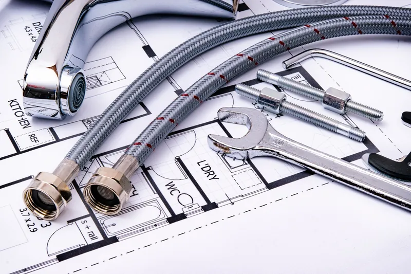 Braided tap hoses, spanners and a pipe wrench lying on a house plan