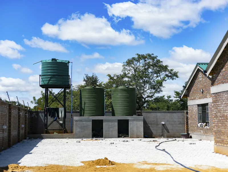 Green water storage tanks on a steel stand beside a brick house